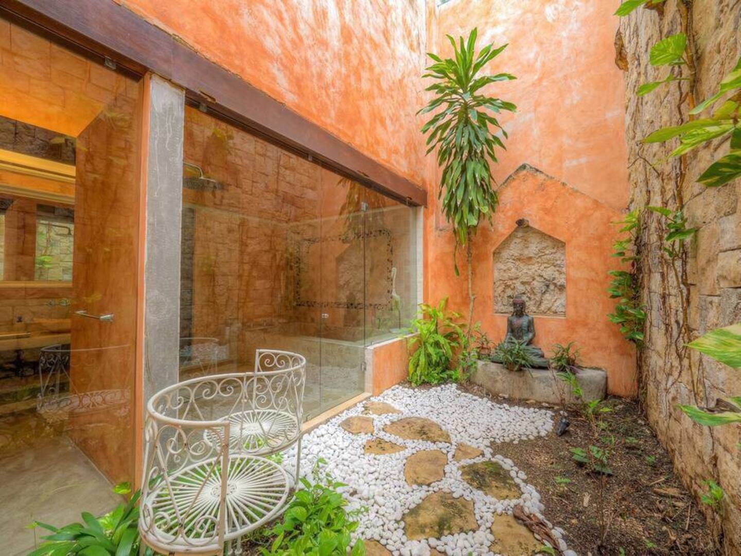 picture of an orange patio, with a metal chair, hanging plants and a statue