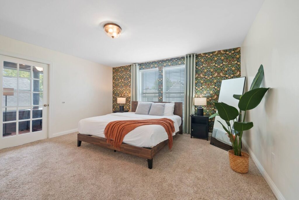 picture of a bedroom with a big bed, a corner mirror and floral wall paper