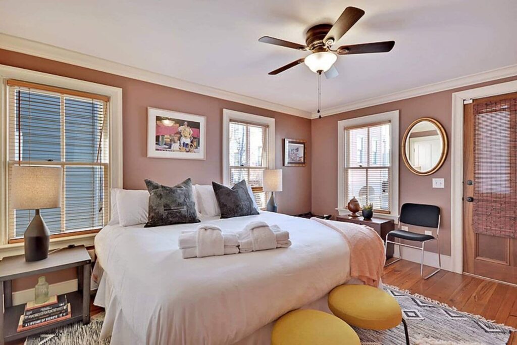 picture of a bedroom, with a bed, dark pink walls, lamps and yellow chairs