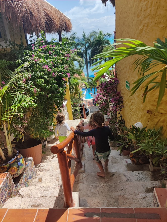 children going down the stairs at a hotel with rock stairs, wooden railing and tropical flowers