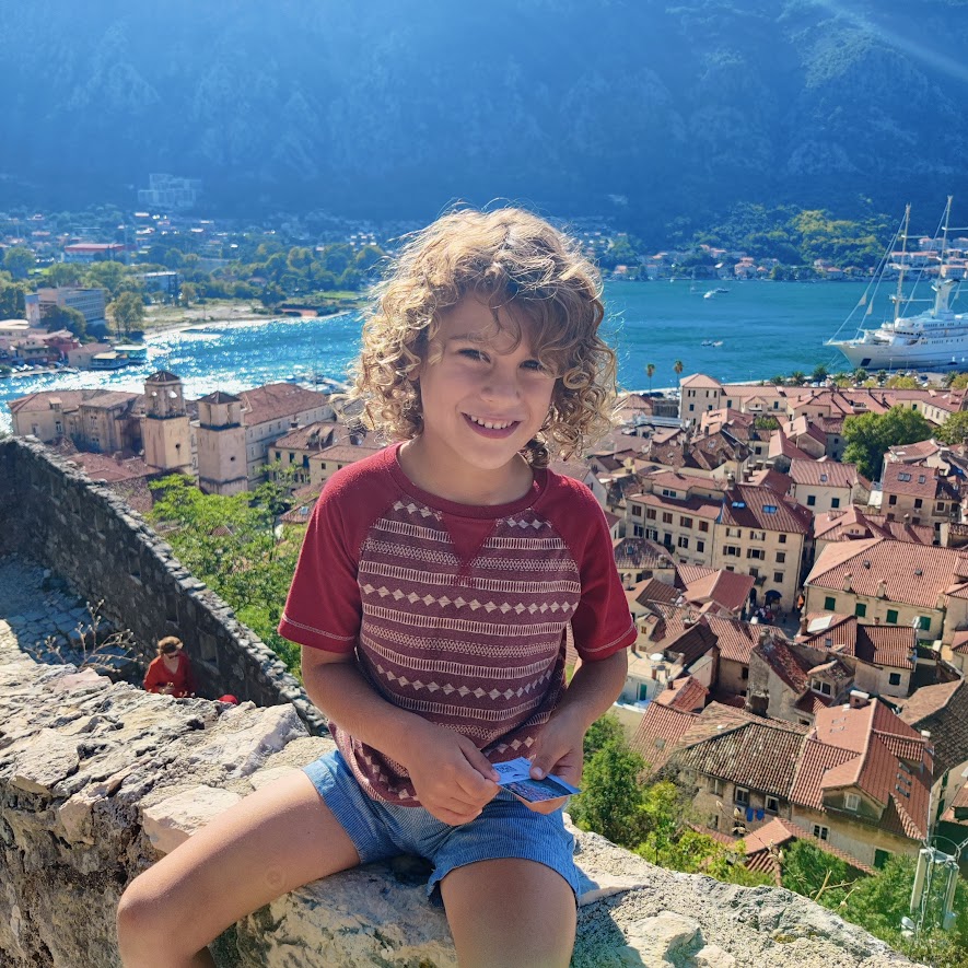 picture of a child smiling while sitting on a wall overlooking a medieval town