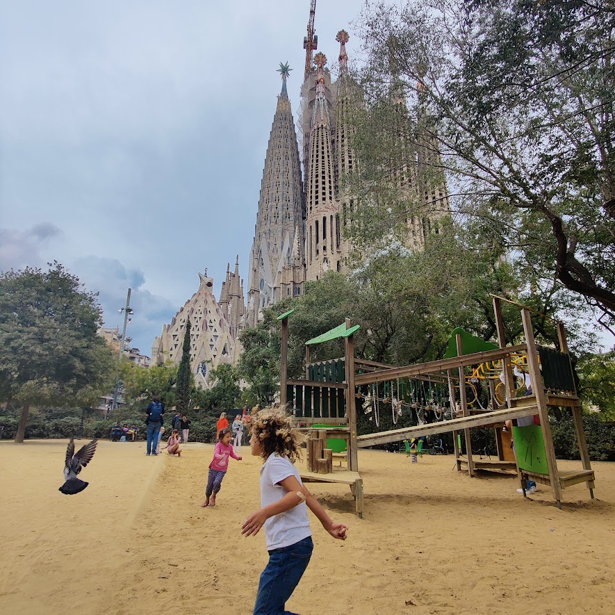 a child playing at a park in front of Sagrada Familia