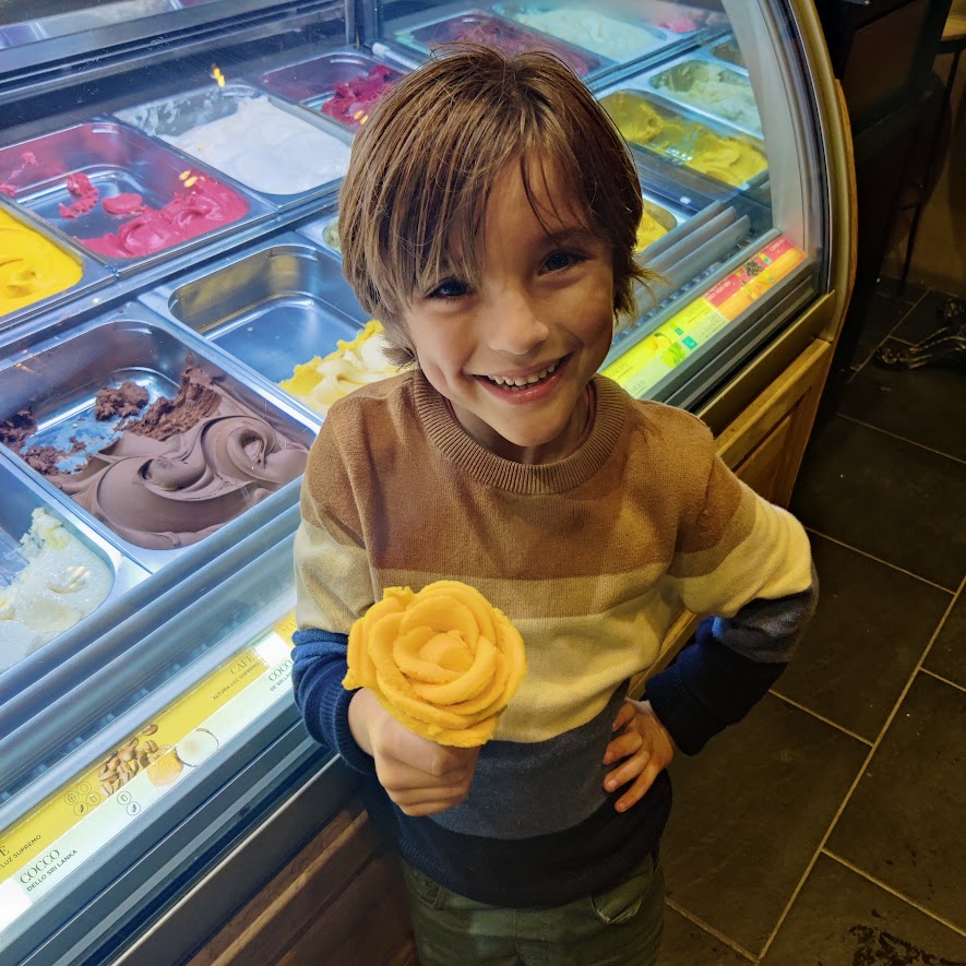 picture of a smiling child holding a yellow ice cream shaped like a rose