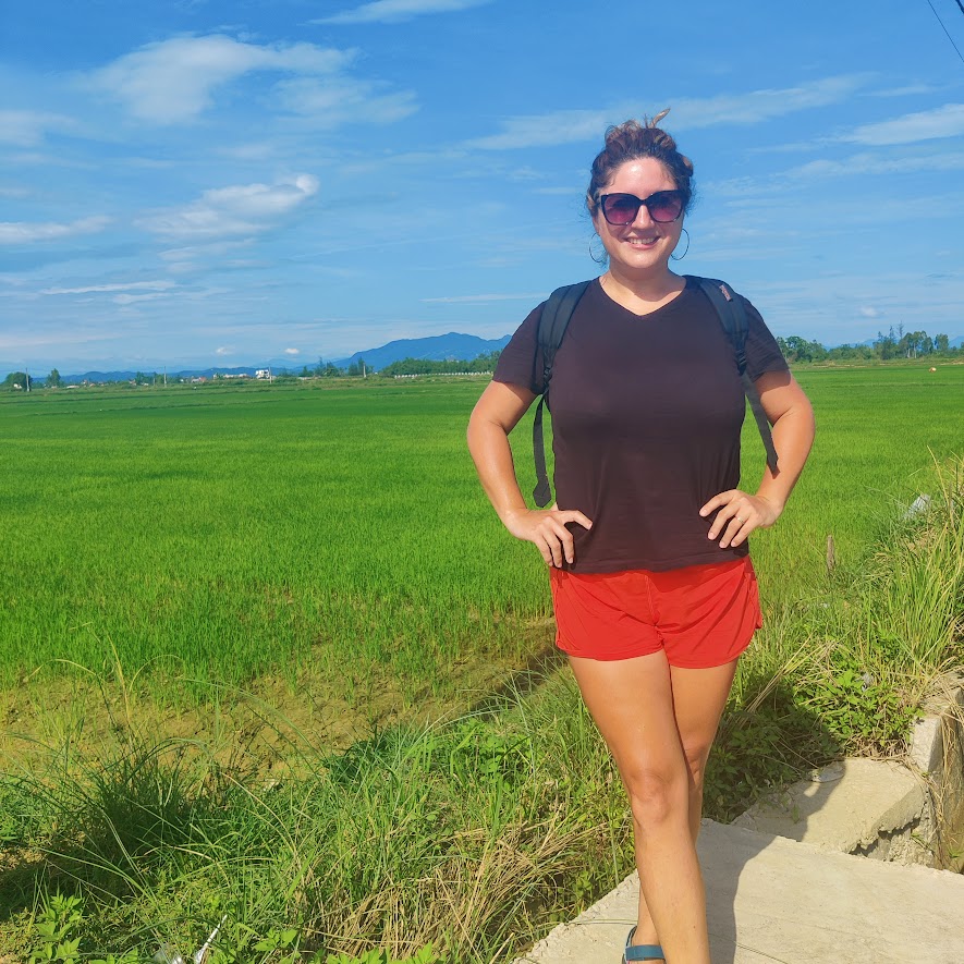 a picture of a woman standing a smiling in front of a rice field