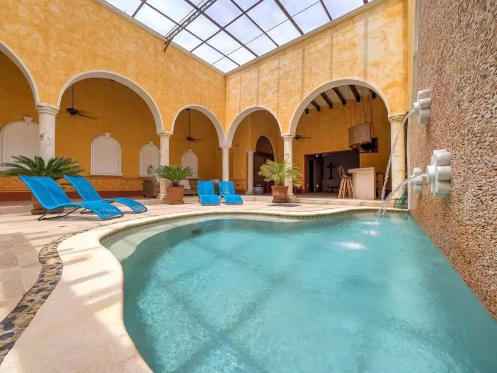 Image of a yellow villa with blue loungers and an indoor covered pool.
