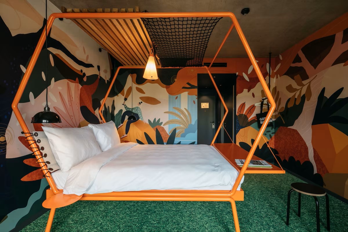 picture of a hotel room with tropical wall paper, green carpet and a bed with wooden bed frame